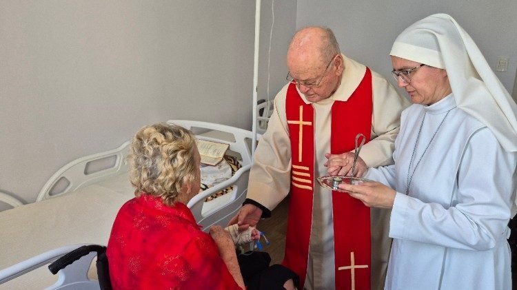 adre Belmiro imparte la unción de los enfermos a una mujer anciana, acompañado de una Pequeña Misionera